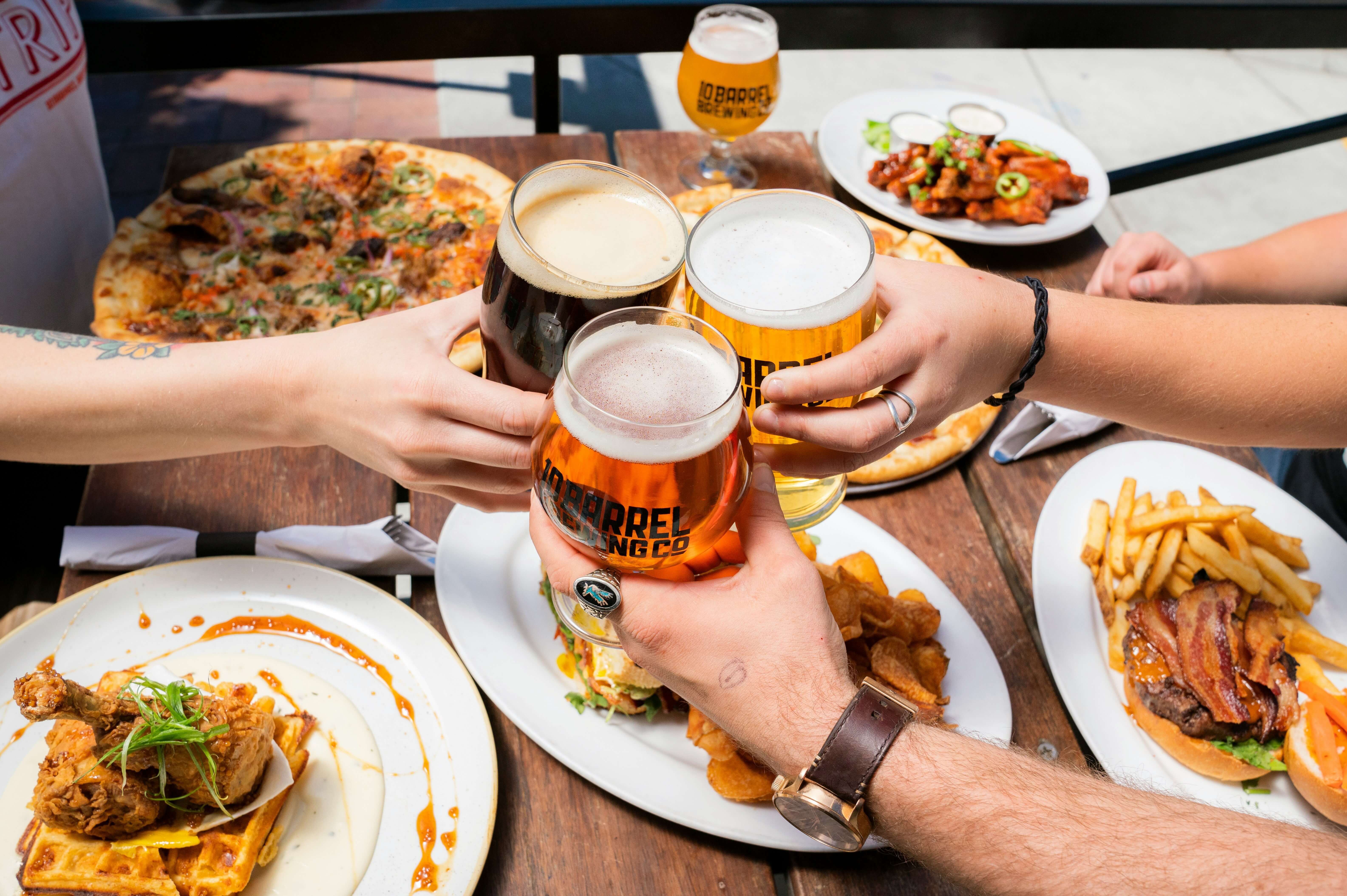 People cheering with beers over plates of food